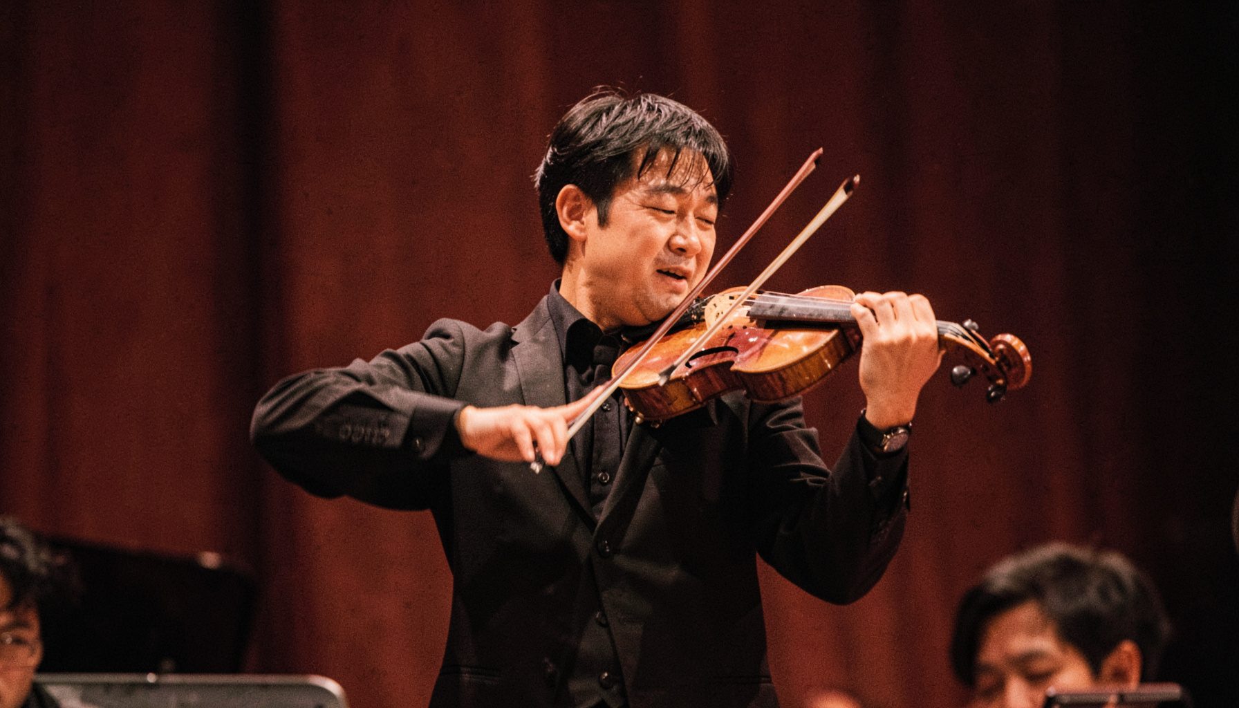 Japanese violinist in concert attire playing with expressive motion, soft amber stage lighting